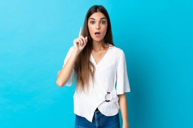 Kafkasyalı genç kadın mavi arka planda izole edildi. Çözümün farkına varmak için parmağını kaldırdı.