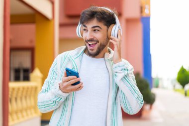 Yakışıklı bir Arap açık havada müzik dinliyor ve şarkı söylüyor.