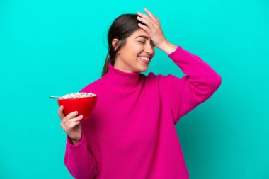 Mavi arka planda bir kase mısır gevreği tutan genç beyaz kadın bir şey fark etti ve çözüme niyetlendi.