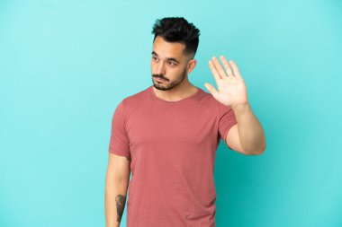 Mavi arka planda izole edilmiş genç beyaz adam dur hareketi yapıyor ve hayal kırıklığına uğruyor.