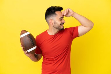 Sarı arka planda izole edilmiş ragbi oynayan genç beyaz adam çok gülümsüyor.