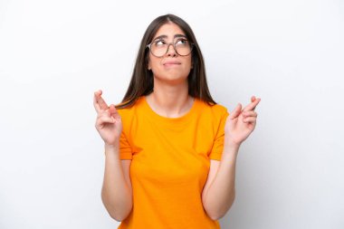 Beyaz arka planda izole edilmiş beyaz tenli genç bir kadın parmaklarını çapraz yapıp en iyisini diliyor.