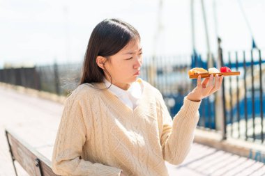 Genç Çinli kadın açık havada sashimi tutuyor, üzgün bir ifadeyle.