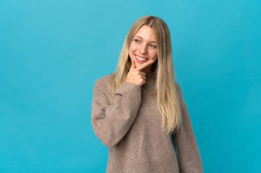Mavi arka planda soyutlanmış genç sarışın kadın yana bakıyor ve gülümsüyor.