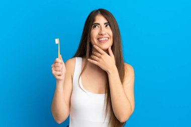 Mavi arka planda dişlerini fırçalayan beyaz bir kadın gülümserken yukarı bakıyor.