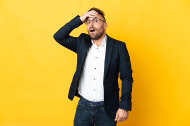 İzole edilmiş sarı arka planda iş adamı, yana bakarken sürpriz jest yapıyor.