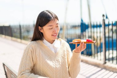 Genç Çinli kadın açık havada saşimi tutuyor, mutlu bir ifadeyle.