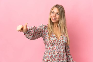 Pembe arka planda izole edilmiş genç sarışın kadın baş parmak işareti yapıyor.