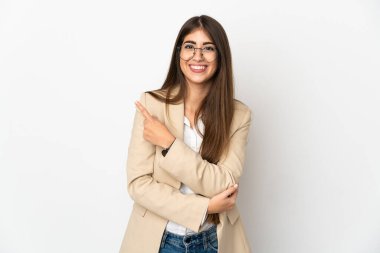 Beyaz arka planda izole edilmiş genç beyaz kadın bir ürünü sunmak için kenarı işaret ediyor.