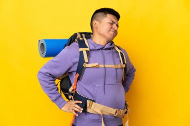 Young mountaineer man with a big backpack isolated on yellow background suffering from backache for having made an effort