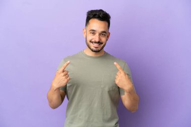 Mor arka planda izole edilmiş genç beyaz bir adam baş parmak hareketi yapıyor.