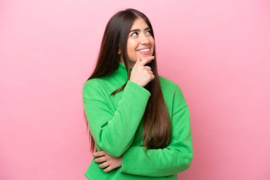 Pembe arka planda soyutlanmış genç beyaz kadın yana bakıyor ve gülümsüyor.