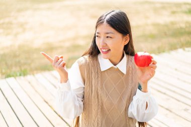 Açık havada elmalı genç bir Çinli kadın bir ürünü sunmak için kenarı işaret ediyor.