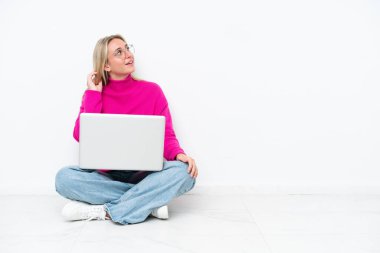 Dizüstü bilgisayarı olan beyaz bir kadın yerde oturmuş bir fikir düşünüyor.