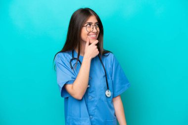 Genç beyaz kadın, mavi arka planda izole edilmiş, yan tarafa bakıyor ve gülümsüyor.