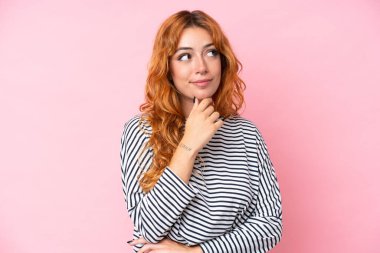 Genç beyaz kadın pembe arka planda izole edilmiş ve yukarı bakıyor.