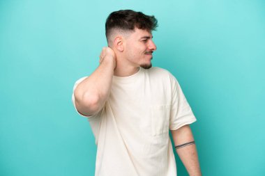 Mavi arka planda boynu ağrıyan, beyaz, yakışıklı genç bir adam.
