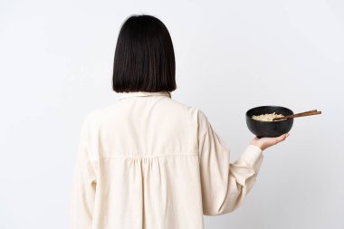 Beyaz arka planda izole edilmiş beyaz tenli genç bir kadın yemek çubuklarıyla bir kase erişte tutarken...