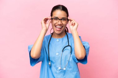 Genç Kolombiyalı hemşire pembe arka planda gözlüklü ve şaşırmış.
