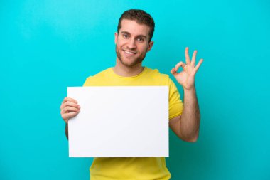 Kafkasyalı genç adam mavi arka planda izole edilmiş, elinde boş bir levha var ve 
