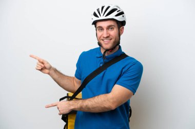 Beyaz arka planda izole edilmiş termal sırt çantalı beyaz tenli genç beyaz bir adam parmak göstererek bir ürün sunuyor.