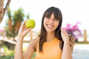 Açık havada elinde mutlu bir ifadeyle elma tutan genç bir kadın.