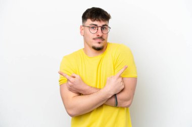 Beyaz arka planda izole edilmiş beyaz tenli yakışıklı genç adam, yan taraftakilerin şüphelerine işaret ediyor.