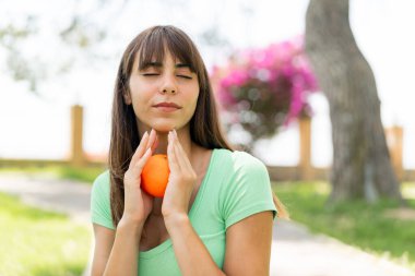 Açık havada elinde portakal tutan genç bir kadın.