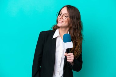 Young TV presenter woman isolated on blue background looking to the side and smiling