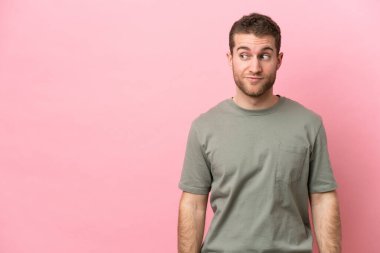 Pembe arka planda izole edilmiş genç beyaz adam şüpheli hareketler yapıyor.