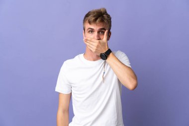Mor arka planda izole edilmiş genç, sarışın bir adam. Ağzını eliyle kapatıyor.