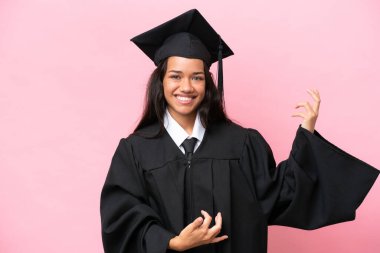 Kolombiyalı genç bir üniversite mezunu pembe arka planda gitar jesti yapıyor.