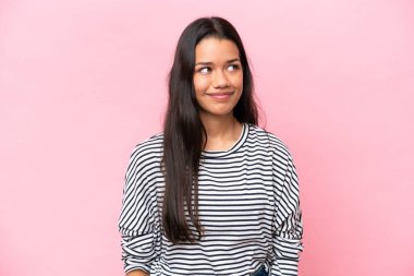 Pembe arka planda izole edilmiş genç Kolombiyalı kadın şüpheli hareketler yapıyor.