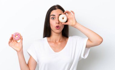 Beyaz arka planda gözünün içinde donut tutan beyaz tenli genç bir kadın.