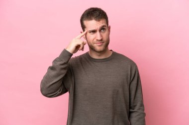 Pembe arka planda izole edilmiş genç beyaz adam deliliğin jestini yapıyor. Parmağını kafaya koyuyor.