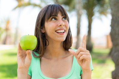 Açık havada elmalı genç bir kadın parmağını kaldırarak çözümü anlamaya çalışıyor.