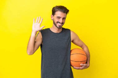 Yakışıklı genç basketbolcu. Sarı arka planda izole edilmiş. Mutlu bir ifadeyle selamlıyor.