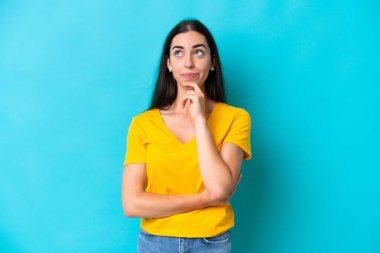 Kafkasyalı genç bir kadın mavi arka planda izole edilmiş. Şüpheleri ve düşünceleri var.