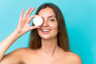 Genç beyaz kadın mavi arka planda izole edilmiş nemlendirici ve mutlulukla