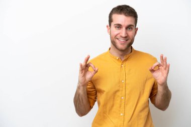 Beyaz arka planda izole edilmiş genç beyaz bir adam iki eliyle tamam işareti gösteriyor.