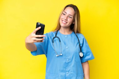 Sarı arka planda izole edilmiş genç cerrah kadın selfie çekiyor.