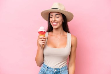 Kornet dondurması olan beyaz bir kadın pembe arka planda izole edilmiş, yana bakıyor ve gülümsüyor.