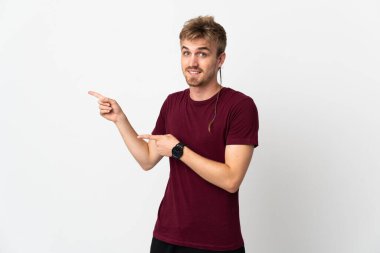Beyaz arka planda soyutlanmış yakışıklı genç adam şaşırmış ve işaret ediyor.