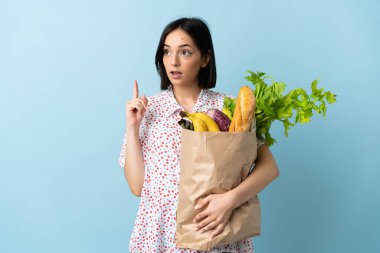 Elinde alışveriş poşeti olan genç bir kadın, bir fikir üzerinde parmak kaldırıyor.