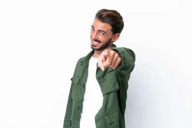 Beyaz arka planda izole edilmiş genç beyaz adam mutlu bir ifadeyle ön tarafı işaret ediyor.