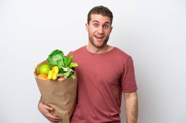 Beyaz arka planda izole edilmiş bir alışveriş torbası tutan beyaz bir adam. Sürpriz bir yüz ifadesi var.