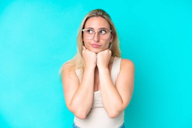 Mavi arka planda, gözlüklü ve yorgun genç beyaz kadın.