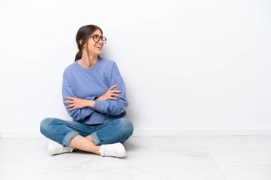 Beyaz arka planda izole bir şekilde yerde oturan beyaz bir kadın mutlu ve gülümsüyor.