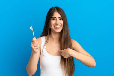 Mavi arka planda diş fırçalayan beyaz bir kadın. Şaşırtıcı bir yüz ifadesi var.