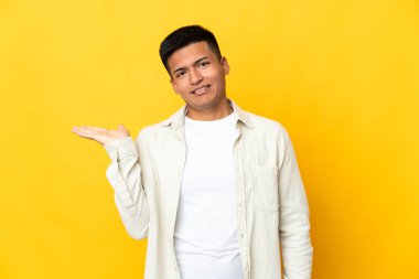 Sarı arka planda izole edilmiş genç Ekvadorlu bir adam bir ilan vermek için avucunun içinde hayali bir fotokopi makinesi tutuyor.